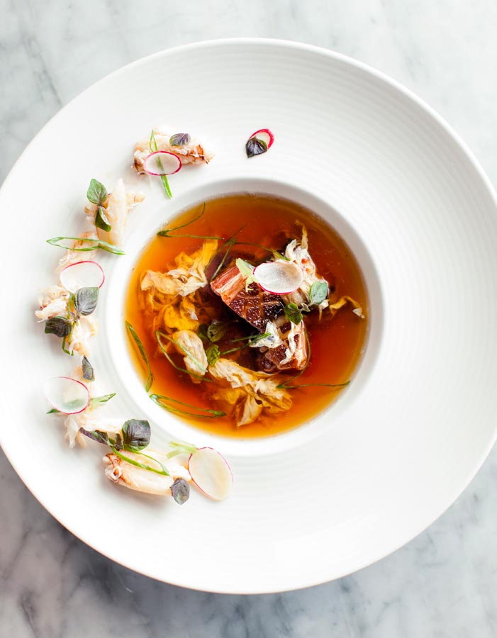 A shellfish consommé being poured over its garnish