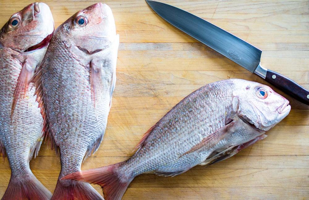 Whole fish on a wooden board beside a chef's knife
